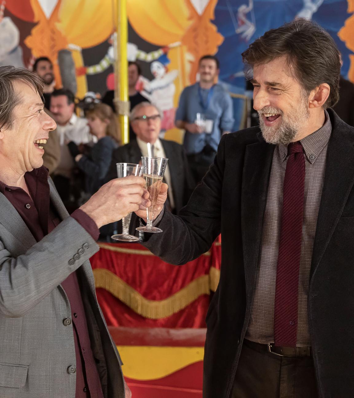 Zwei Männer mit Sektgläsern in der Hand prosten sich lachend zu.