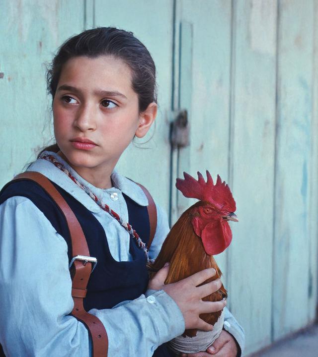 Ein Mädchen hält einen Hahn auf dem Arm.