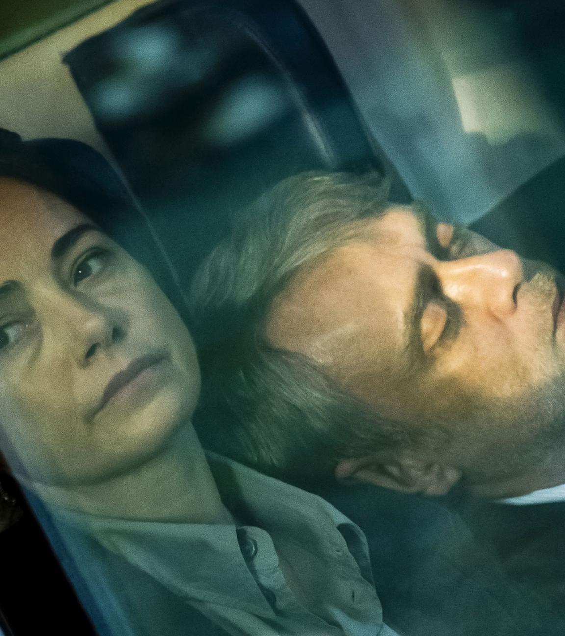 Eine Frau schaut aus einem Fenster, an ihrer Schulter lehnt ein Mann mit geschlossenen Augen.