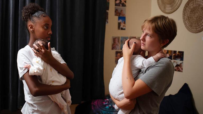 Zwei junge Frauen stehen sich gegenüber und halten ihre Babies auf dem Arm.