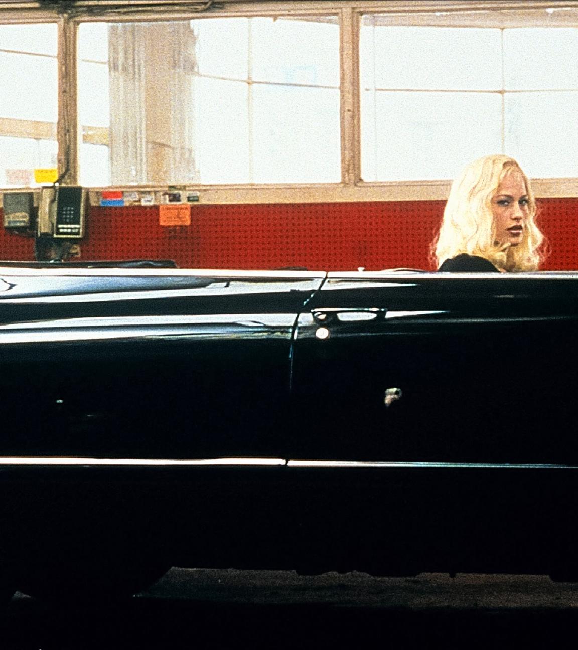 Eine blonde Frau sitzt in einem schwarzen Oldtimer-Cabrio.