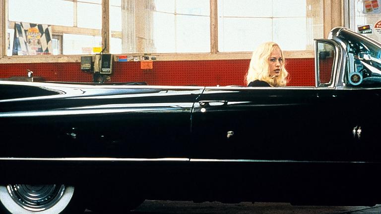 Eine blonde Frau sitzt in einem schwarzen Oldtimer-Cabrio.