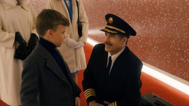 Ein Flugkapitän in Uniform kniet sich nieder, um mit einem kleinen Jungen in einer altmodischen Anzugjacke zu sprechen.