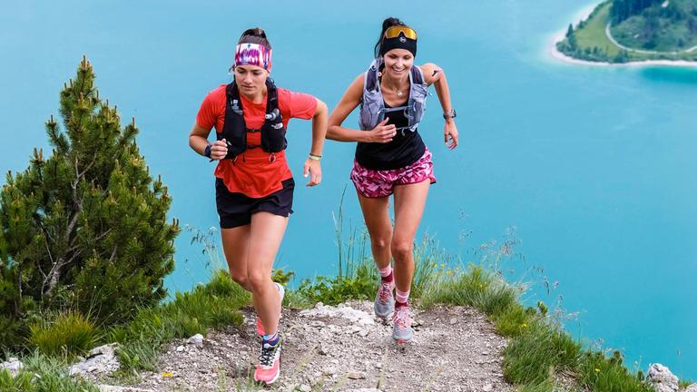 Zwei Frauen in Sportbekleidung laufen auf einem Bergweg.