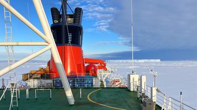 Blick von einem Eisbrecher auf das Polarmeer, auf dem eine Eisschicht liegt.
