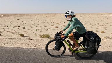 Eine Frau fährt mit dem Fahrrad durch die Wüste.