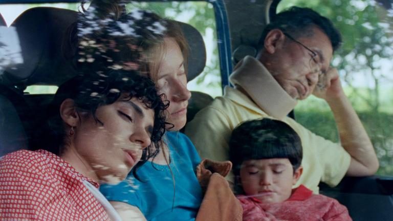 Auf der Rückbank eines Autos sitzen ein Mann, zwei Frauen und ein Kind und schlafen.