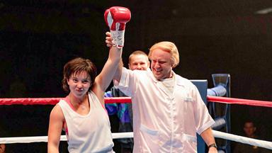 In einem Boxring hebt ein Mann den Arm der siegreichen jungen Boxerin.