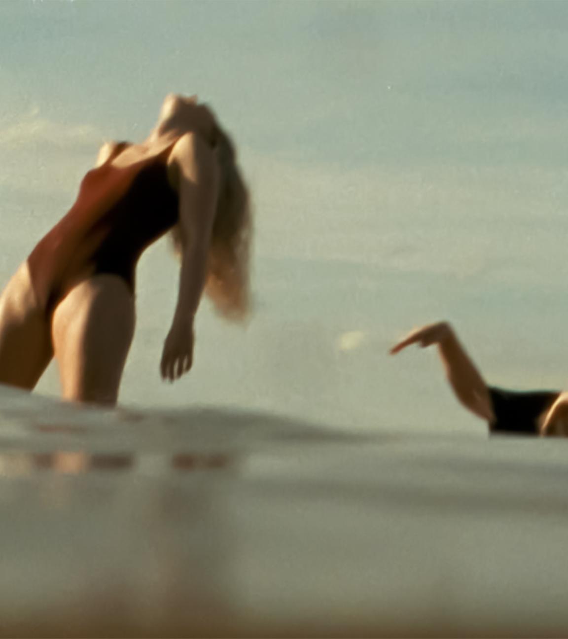 Zwei Frauen im Meer, eine steht, eine badet.