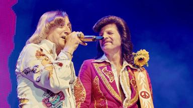 Zwei Männer in Kostümen der 1970er Jahre stehen auf der Bühne und singen.