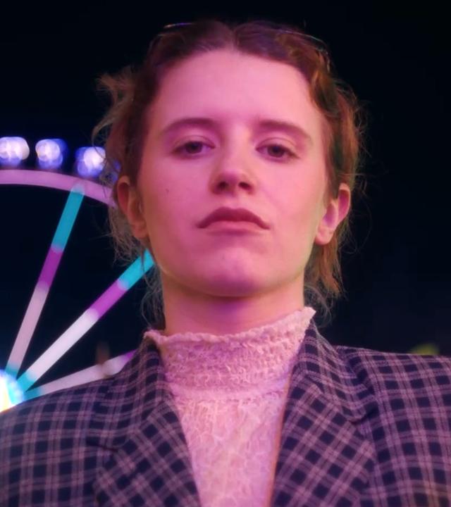 Eine Frau steht auf dem Jahrmarkt vor einem Riesenrad.