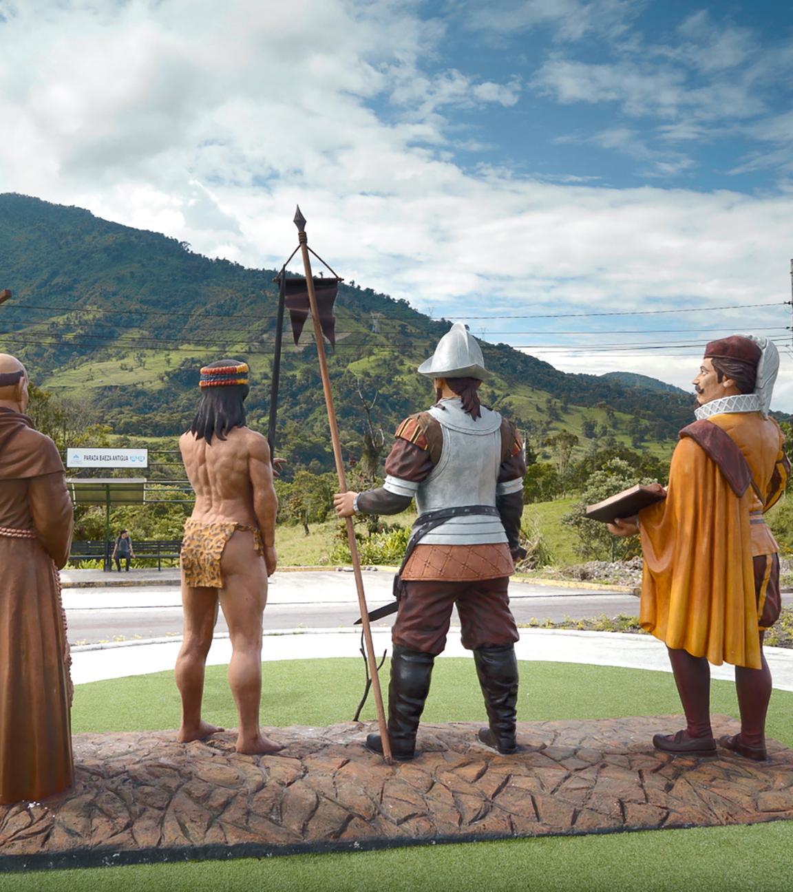 Vier Figuren stehen als Skulpturen in der Landschaft.