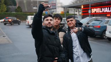 Drei junge Männer machen ein Foto von sich vor einer Spielhalle.