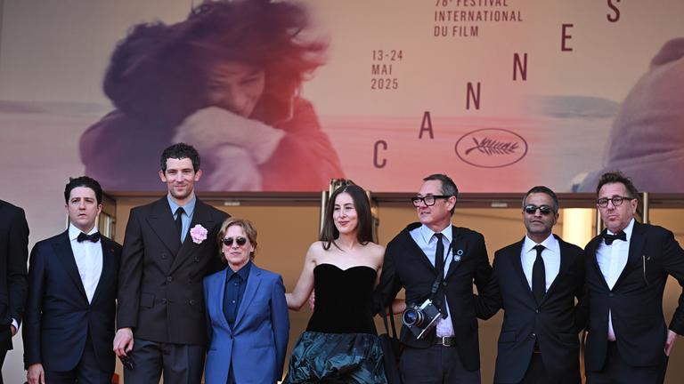 Mehrere Personen der Filmbranche stehen vor einem Plakat der Cannes Filmfestspiele