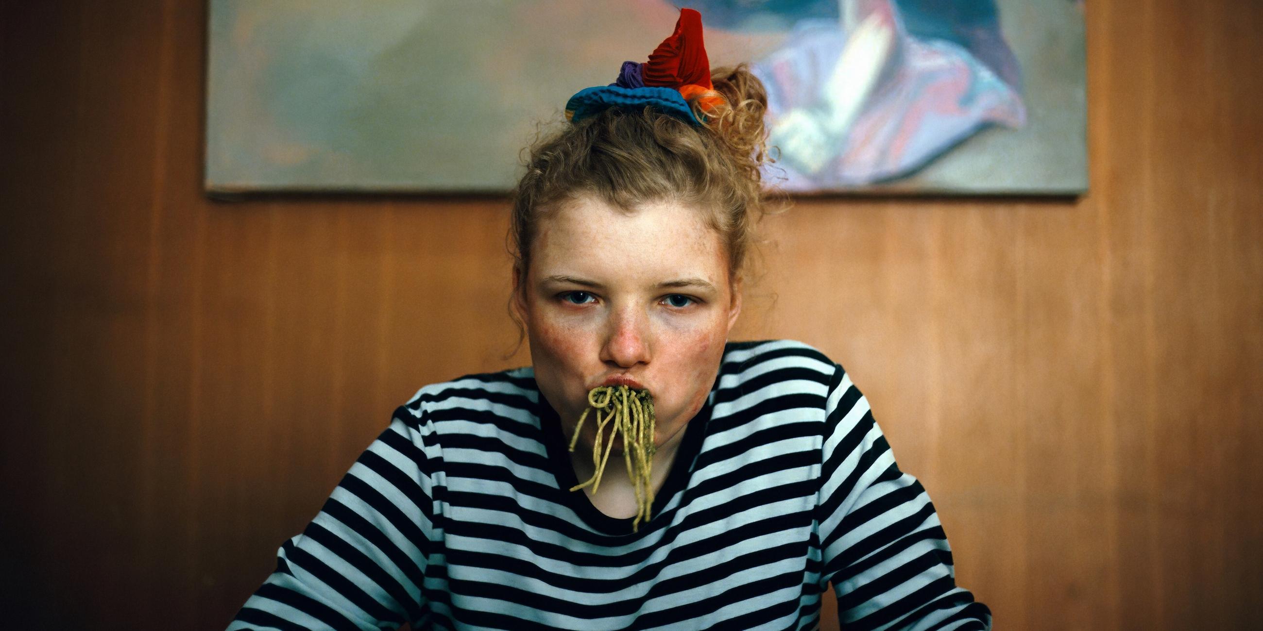 Eine junge Frau hat sich den Mund mit Spaghetti vollgestopft und blickt grimmig in die Kamera.