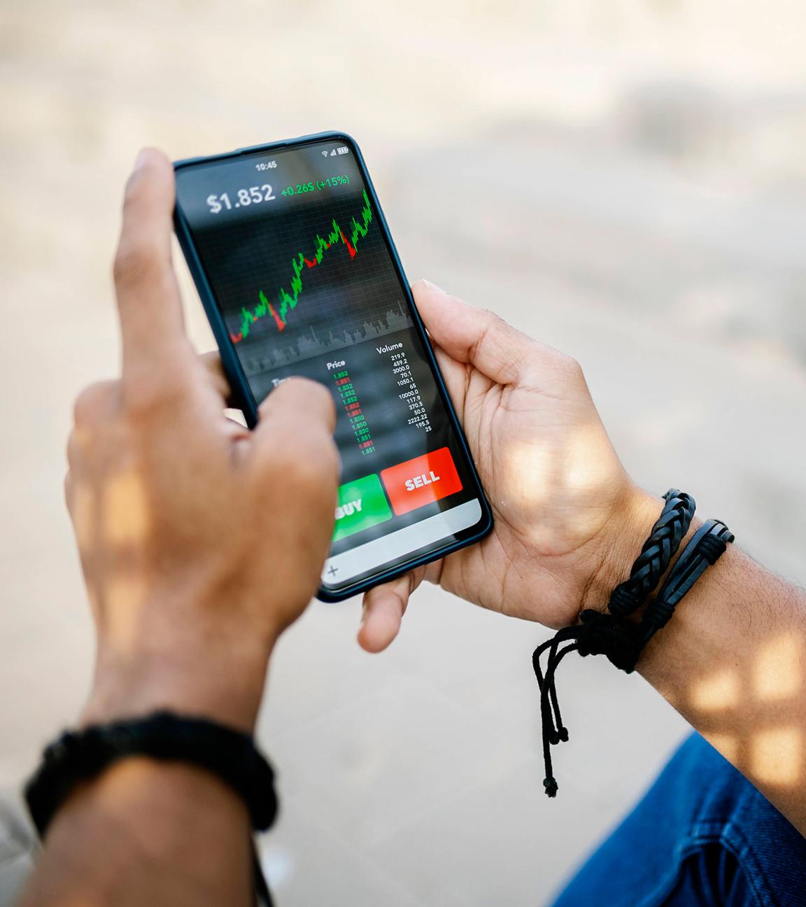 Eine Person hält ein Handy mit Aktienkursen auf dem Bildschirm in der Hand.