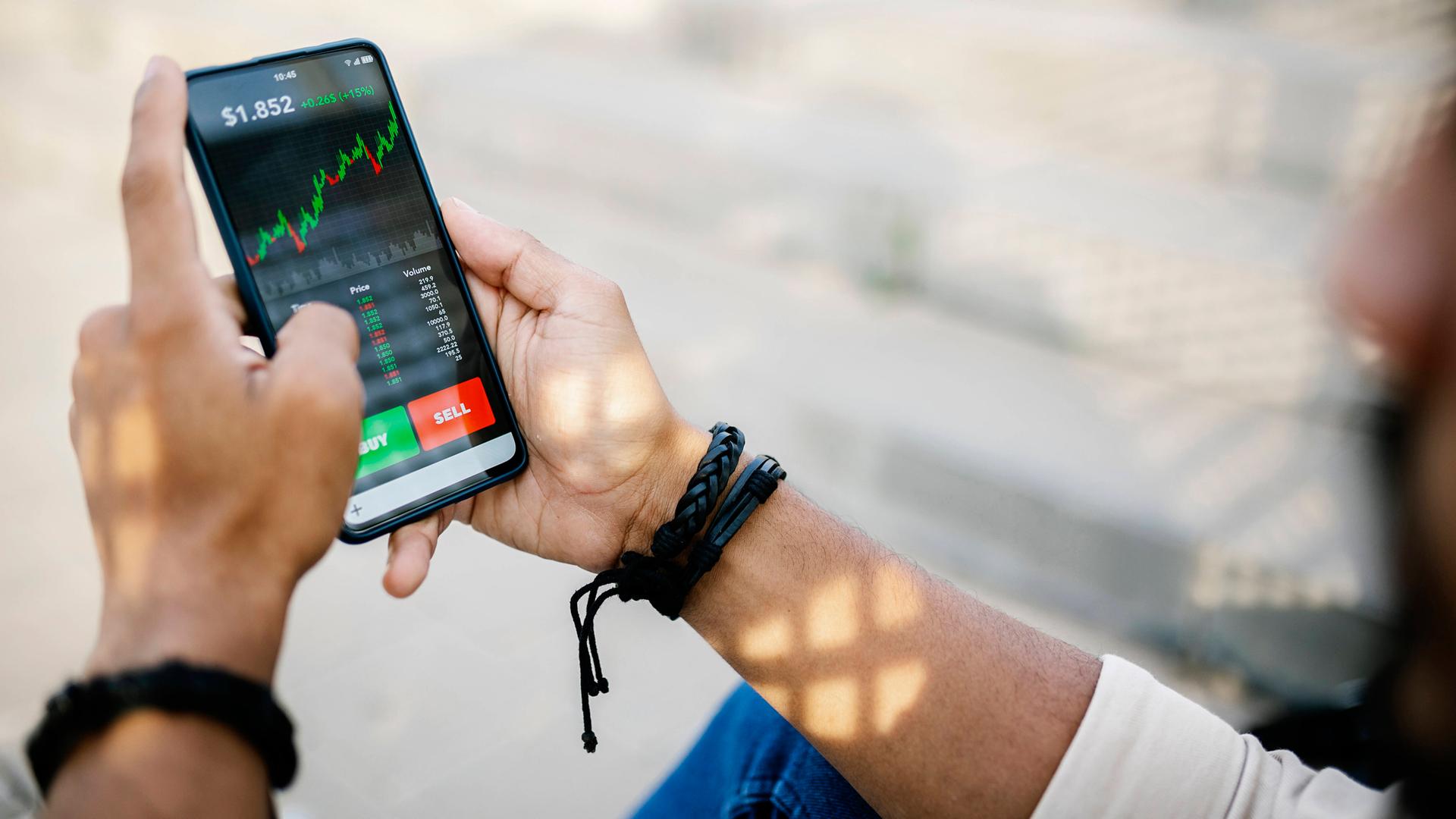 Eine Person hält ein Handy mit Aktienkursen auf dem Bildschirm in der Hand.