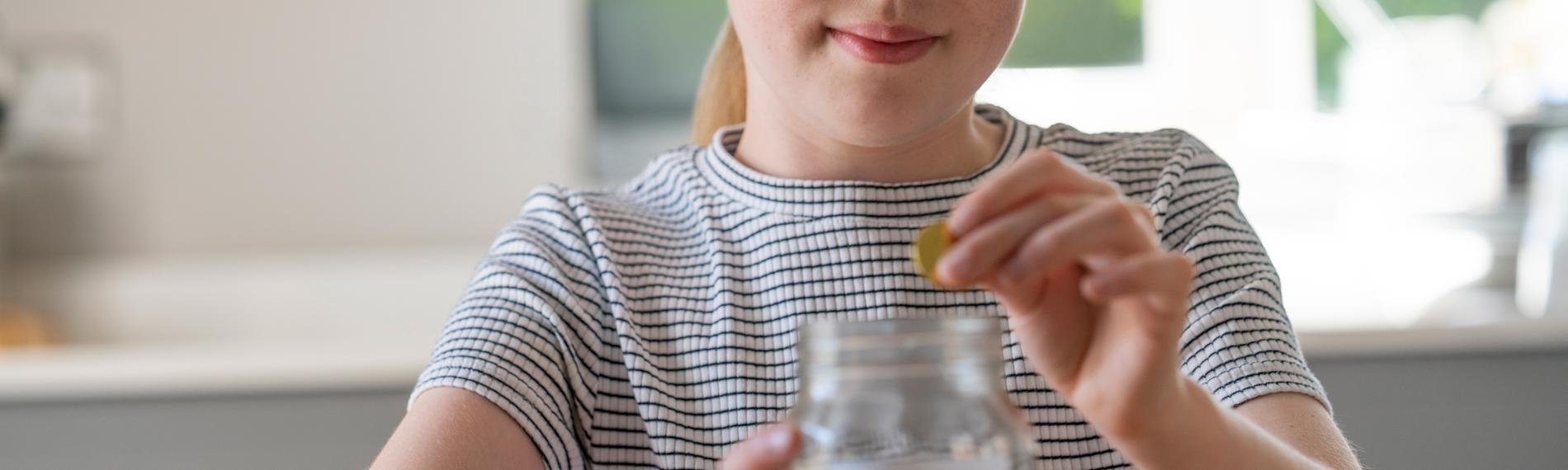 Ein Mädchen wirft Geld in ein Glas.