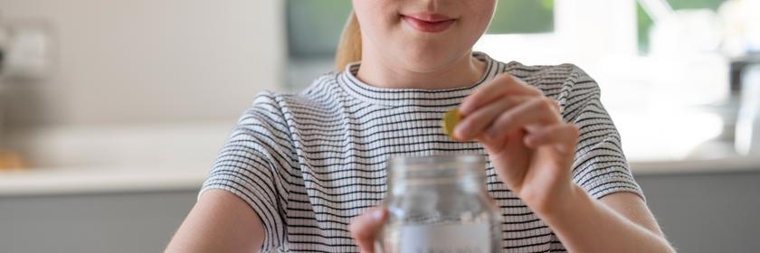 Ein Mädchen wirft Geld in ein Glas.