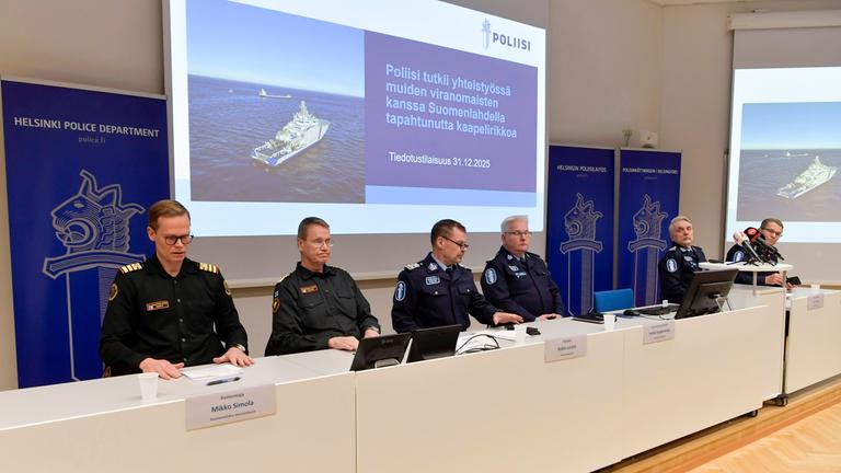 Vier Beamte sitzen vor einer Präsentation bei einer Pressekonferenz in Helsinki zu einem zerstörten Untersee-Kabel.