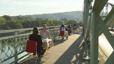 Personen sitzen an Tischen auf einer Brücke und frühstücken