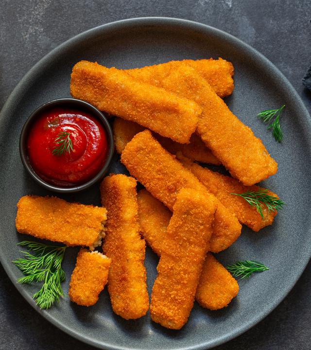 Frittierte Fischstäbchen mit Ketchup auf einem grauen Teller serviert.