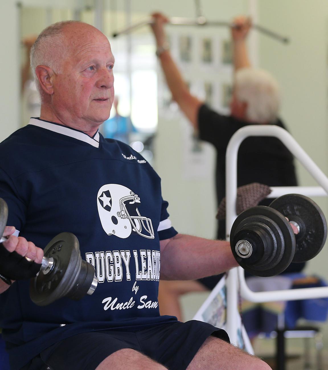 Älterer Herr sitzt in einem Fitnessstudio und macht Hantelübungen.