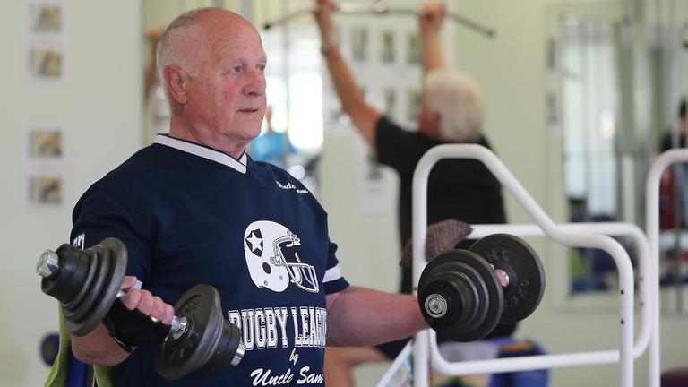 Älterer Herr sitzt in einem Fitnessstudio und macht Hantelübungen.