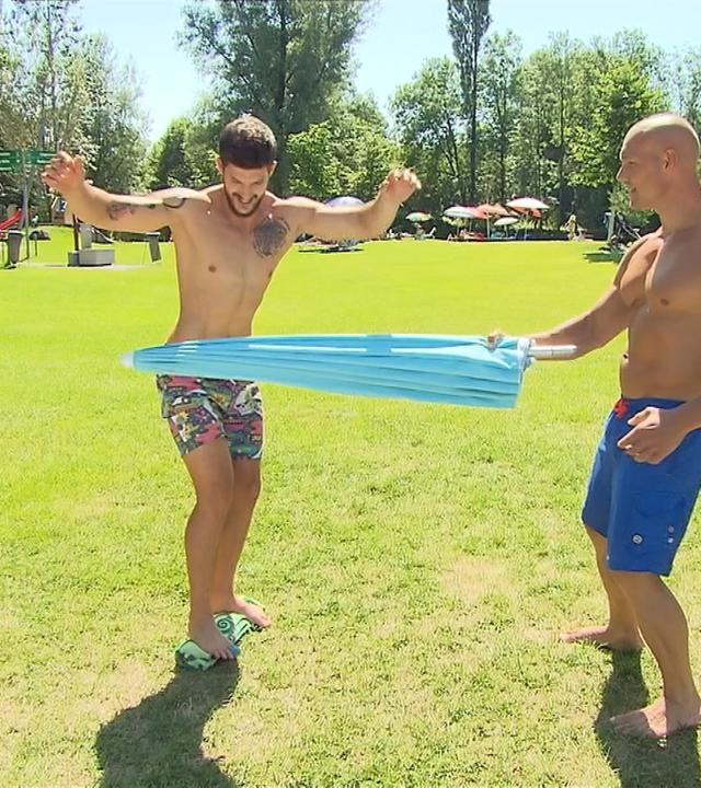 Zwei Männer machen eine Sportübung mit einem Sonnenschirm