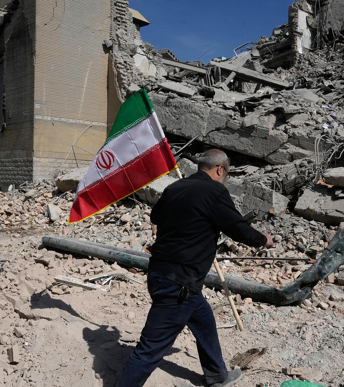 Ein Mann trägt eine iranische Flagge zu den Trümmern einer Polizeiwache