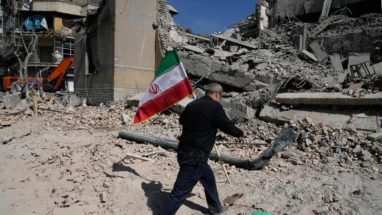 Ein Mann trägt eine iranische Flagge zu den Trümmern einer Polizeiwache