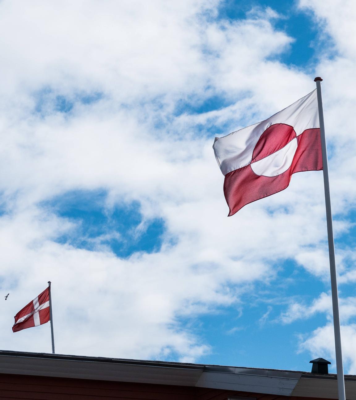 Die dänische und grönländische Flagge weht bei blauem Himmel in Grönland.