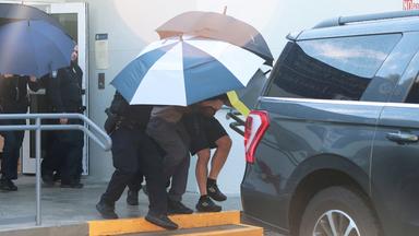 Flavio Bolsonaro wird mittels Regenschirmen abgeschirmt.