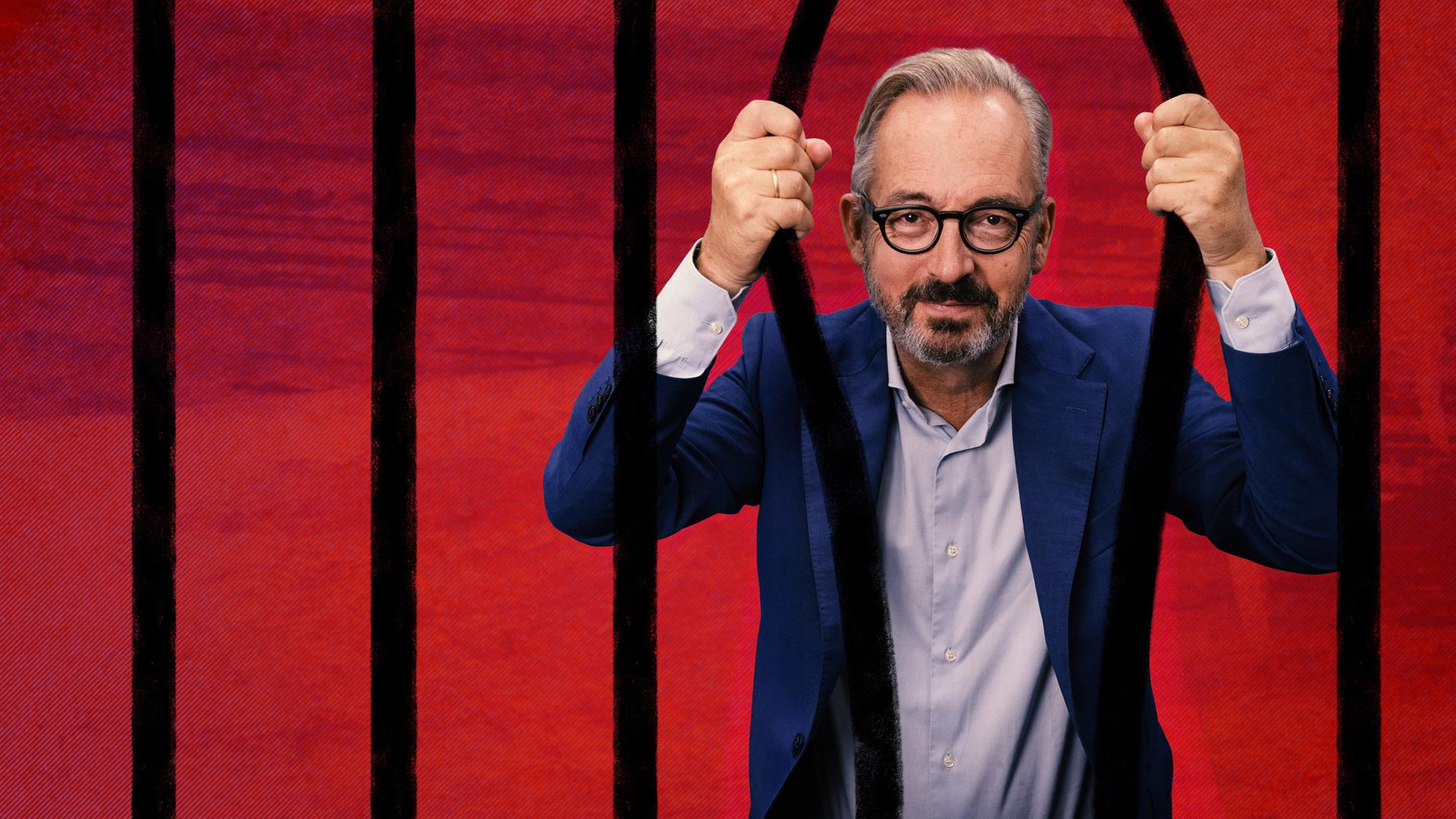 „Keine Talkshow - Eingesperrt mit Jan Fleischhauer“: Fleischhauer hält sich mit den Händen von hinten an zwei Stäben vor einem roten HIntergrund fest und schaut direkt in die Kamera.