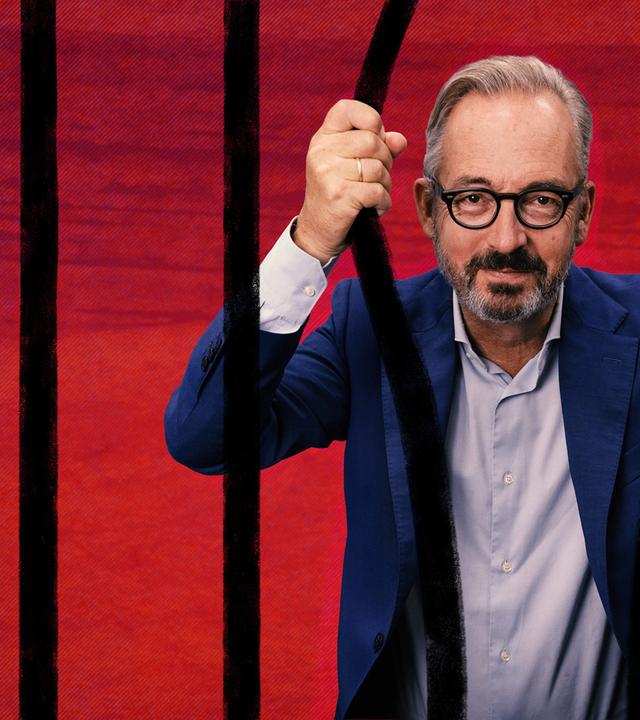 „Keine Talkshow - Eingesperrt mit Jan Fleischhauer“: Fleischhauer hält sich mit den Händen von hinten an zwei Stäben vor einem roten HIntergrund fest und schaut direkt in die Kamera.