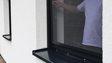 Ein Mann montiert ein Fliegengitter an einem Fenster.