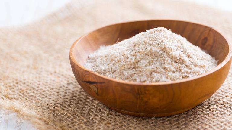 Ein Haufen von Flohsamen in einer Holzschale auf einem Holztisch.