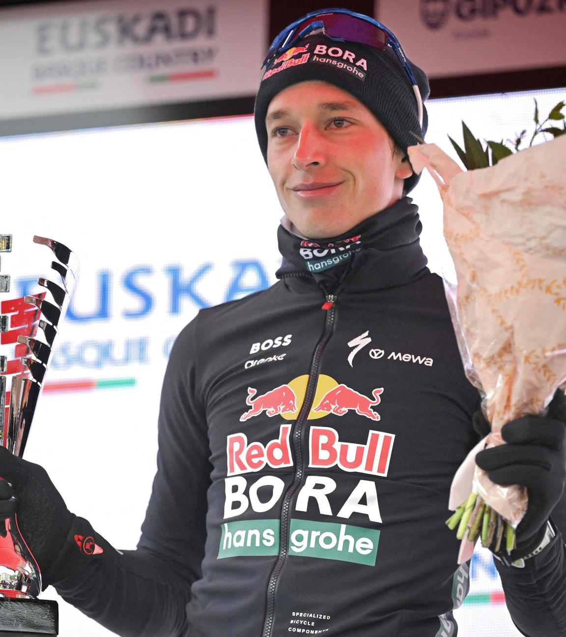 Florian Lipowitz bei der Siegerehrung der Baskenland-Rundfahrt mit einem Pokal in der rechten und einen Blumenstrauß in der linken Hand.