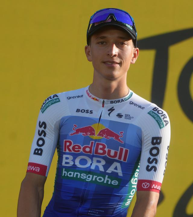 Florian Lipowitz steht in Fahrradmontur vor einem gelben Hintergrund.