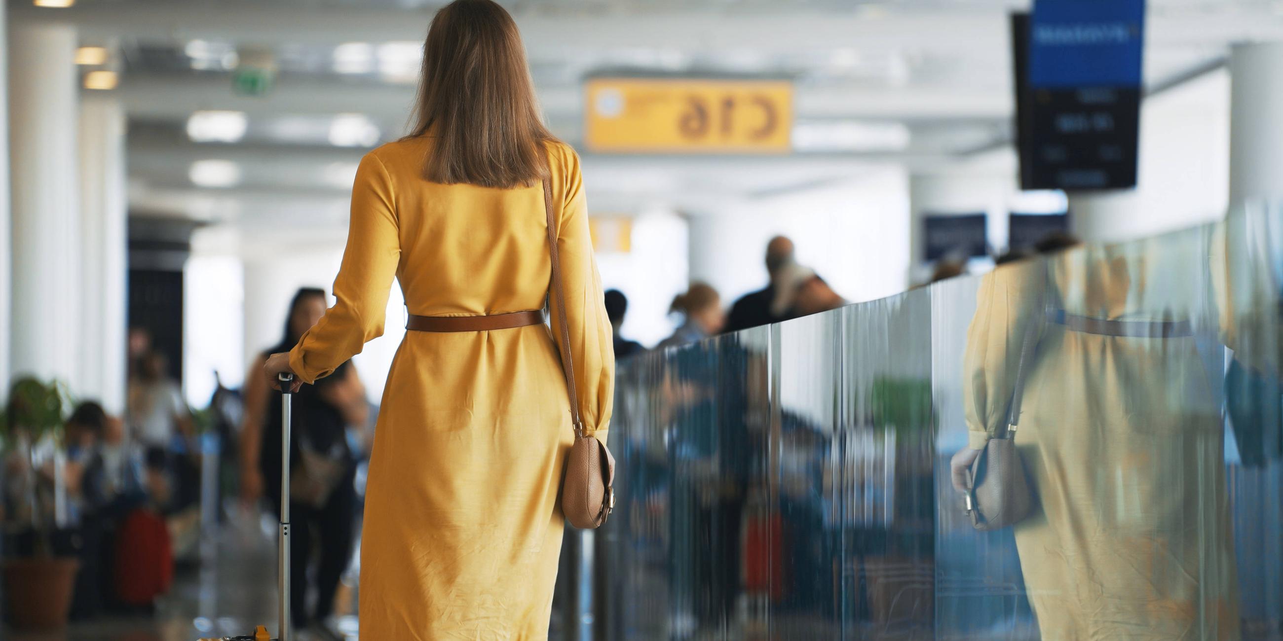 Eine Frau geht mit ihrem Koffer zu ihrem Abfluggate im Flughafen-Terminal.