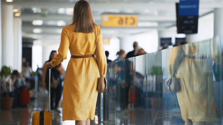 Eine Frau geht mit ihrem Koffer zu ihrem Abfluggate im Flughafen-Terminal.