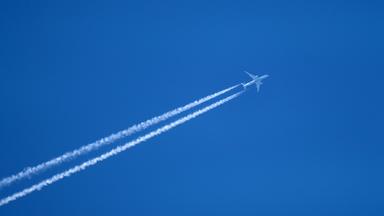 Flugzeug hinterlässt Kondensstreifen am Himmel.