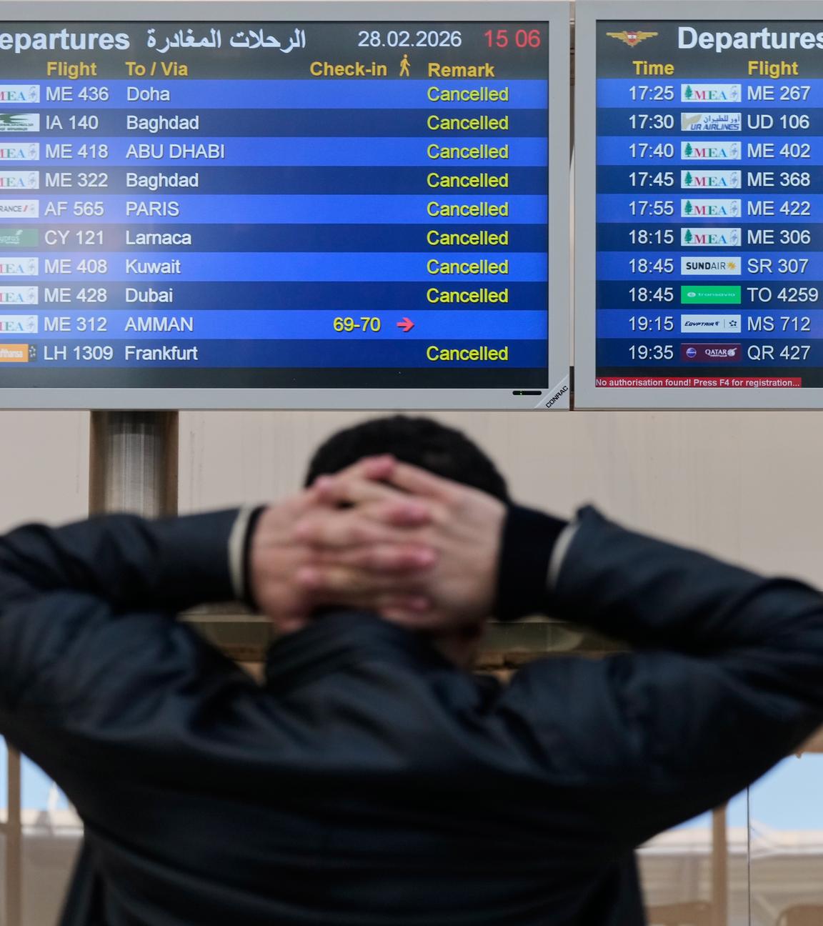 Ein Mann (von hinten zu sehen) schaut auf die Anzeigetafel am Flughafen Beirut im Libanon und verschränkt die Hände hinter dem Kopf.