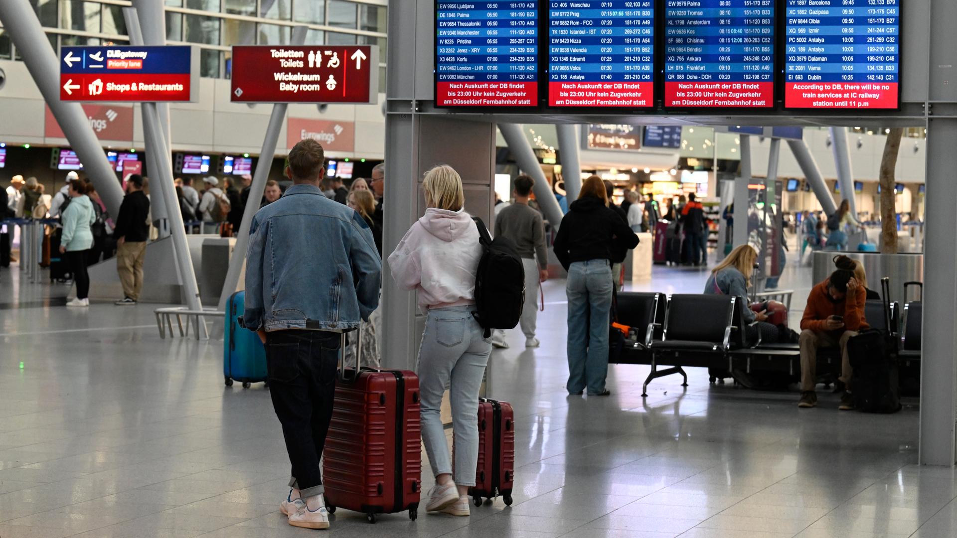 Reisende mit Gepäck gehen in der Abflughalle des Flughafens Düsseldorf.
