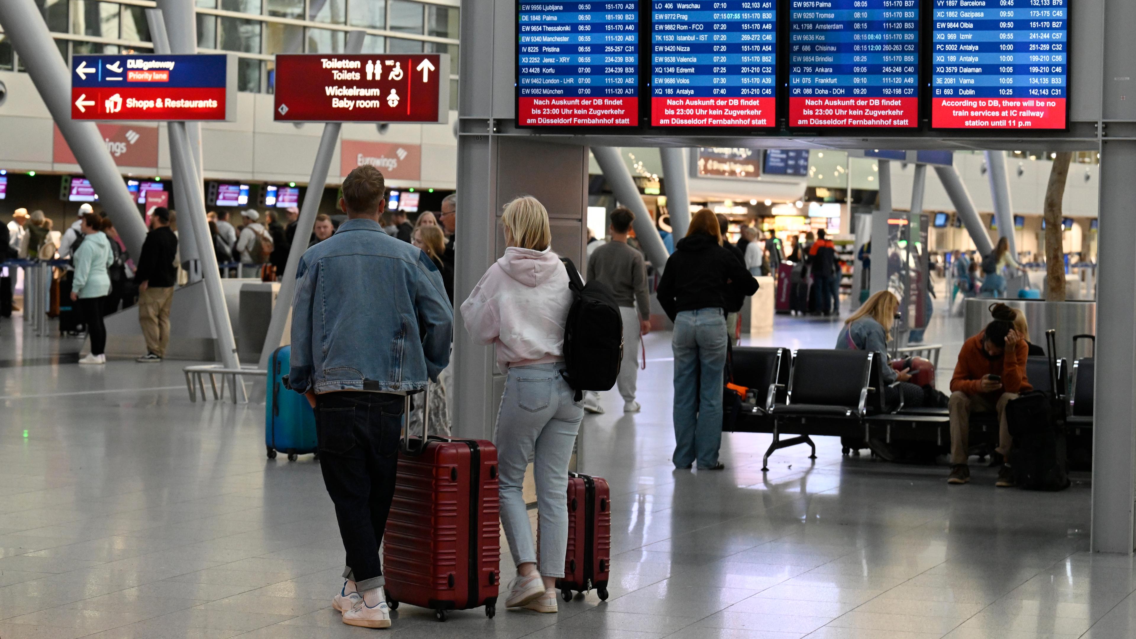 Reisende mit Gepäck gehen in der Abflughalle des Flughafens Düsseldorf.
