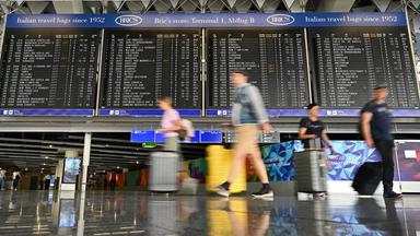 Urlauber laufen im Terminal 1 an einer großen Anzeigetafel vorbei. 