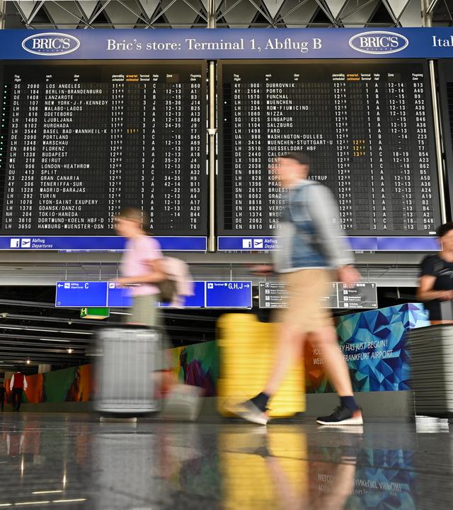 Urlauber laufen im Terminal 1 an einer großen Anzeigetafel vorbei. 