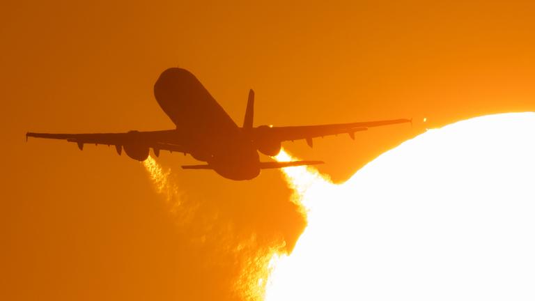 (Archiv) Ein Flugzeug startet vom Flughafen Frankfurt und fliegt dabei an der untergehenden Sonne vorbei.