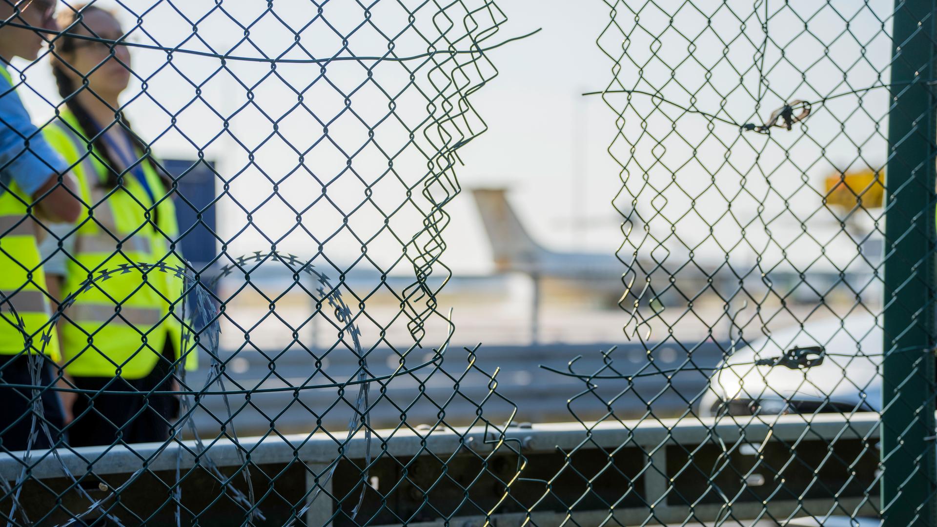 raport-Mitarbeiter stehen an dem zerstörten Zaunabschnitt, durch den die Klima-Aktivisten auf das Flughafengelände eingedrungen sind.