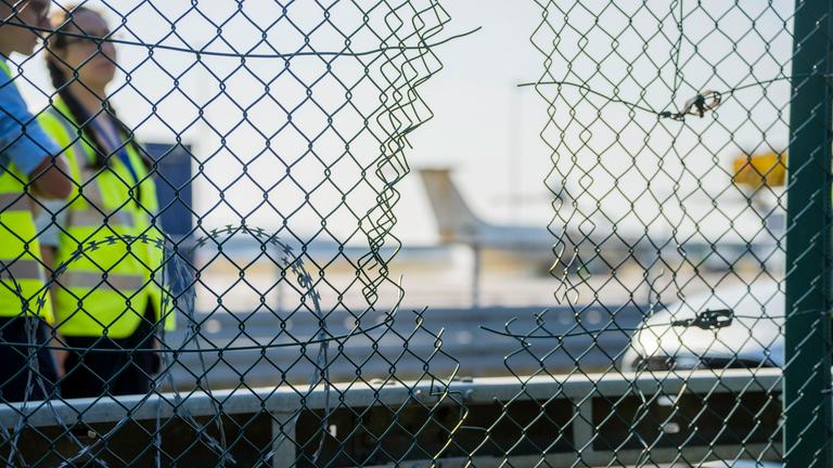 raport-Mitarbeiter stehen an dem zerstörten Zaunabschnitt, durch den die Klima-Aktivisten auf das Flughafengelände eingedrungen sind.